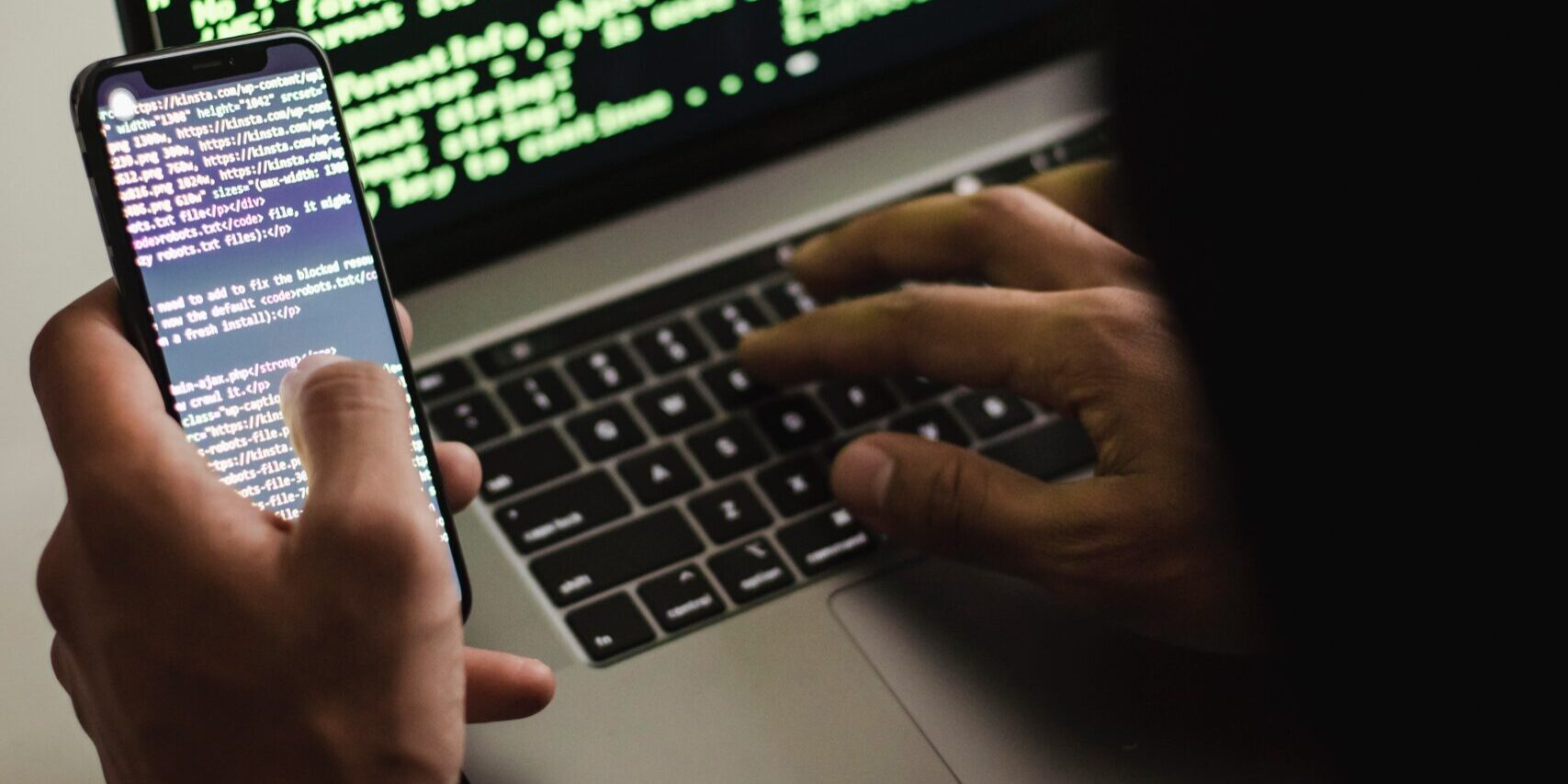 Free Unrecognizable hacker with smartphone typing on laptop at desk Stock Photo